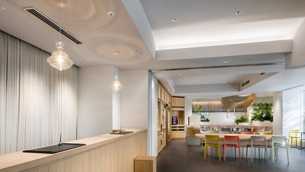 A modern interior with a wooden reception desk, a dining area with colorful chairs, and a kitchen with plants. - Tokyu Stay Ikebukuro (Tokyo)