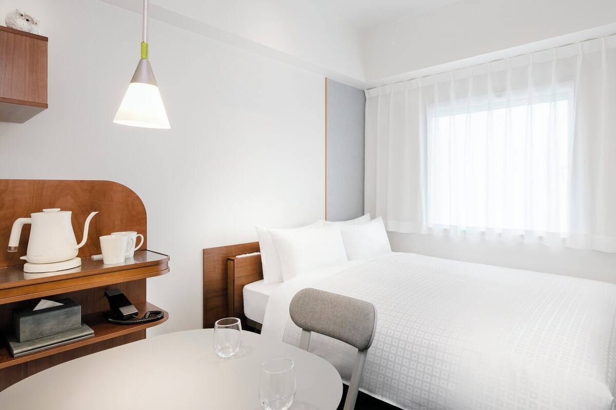 A hotel room with a bed, bedside table, lamp, and a TV.