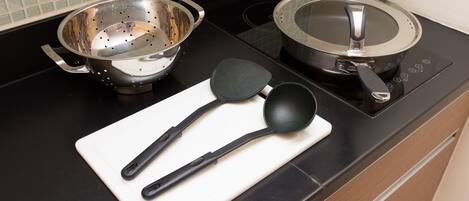 A kitchen counter with a colander, a frying pan, and a spatula on a cutting board.