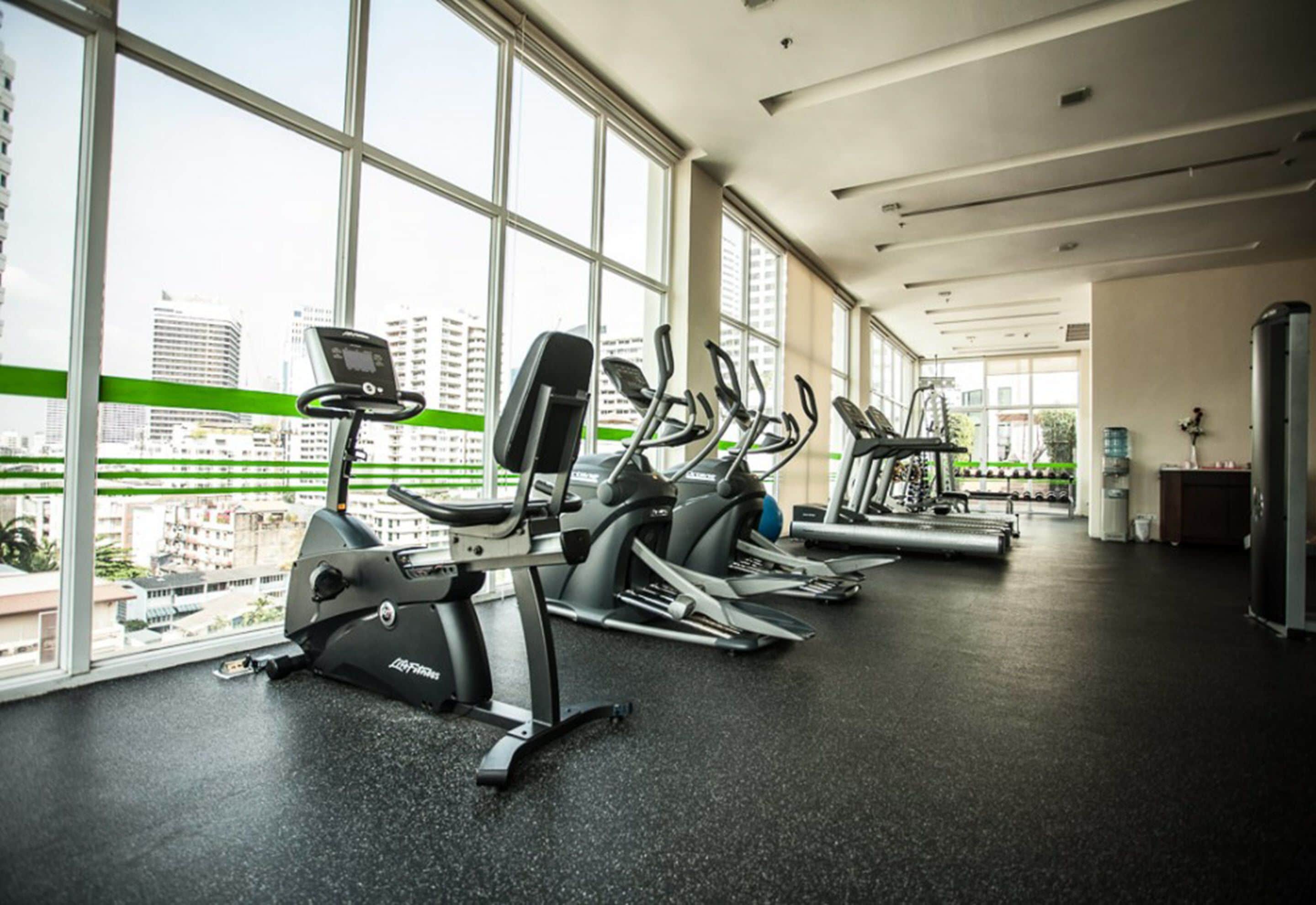 Un gimnasio con máquinas de cardio y vistas a la ciudad a través de amplios ventanales.