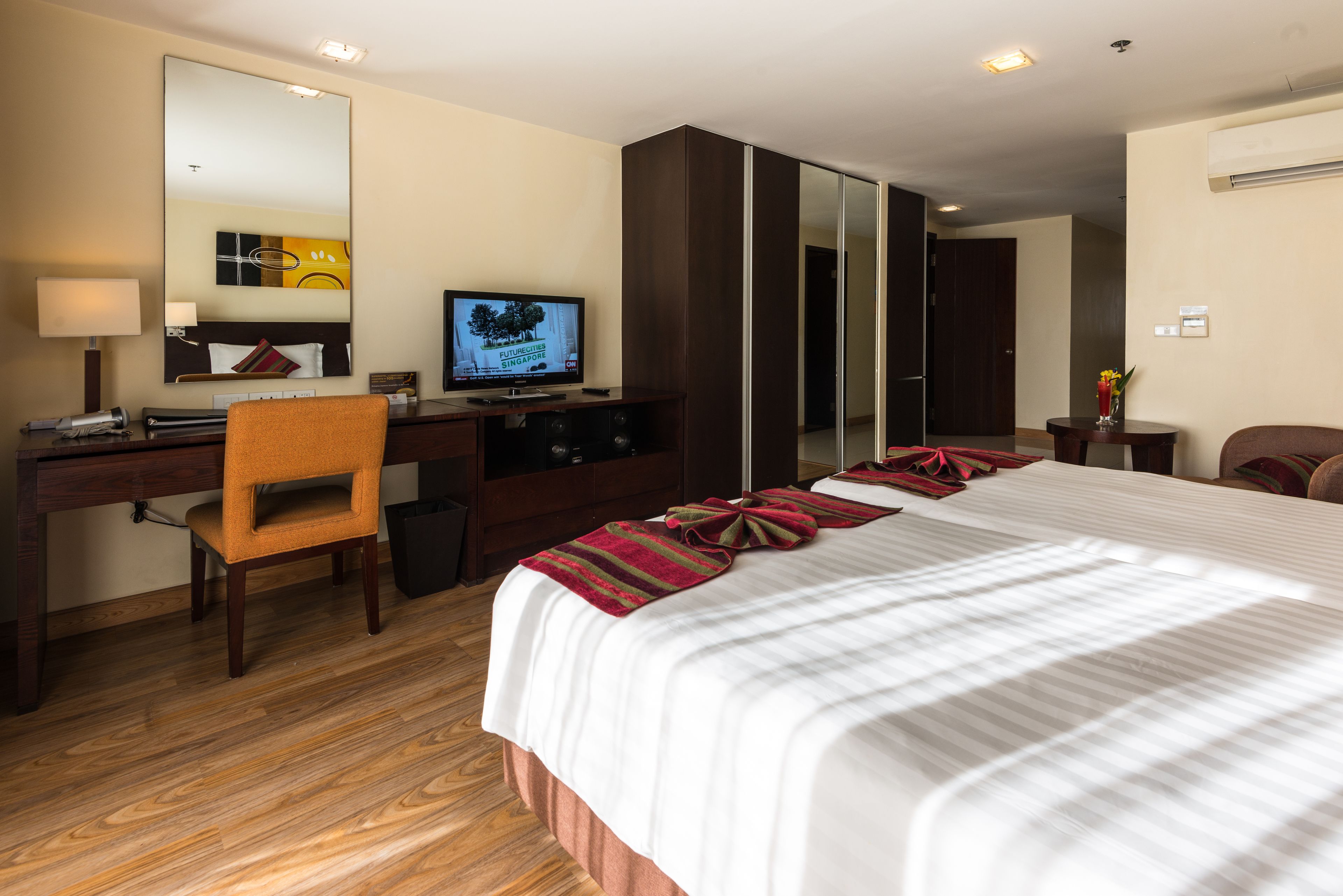 A hotel room with a large bed, a desk with a computer, a chair, a TV, and a wardrobe.