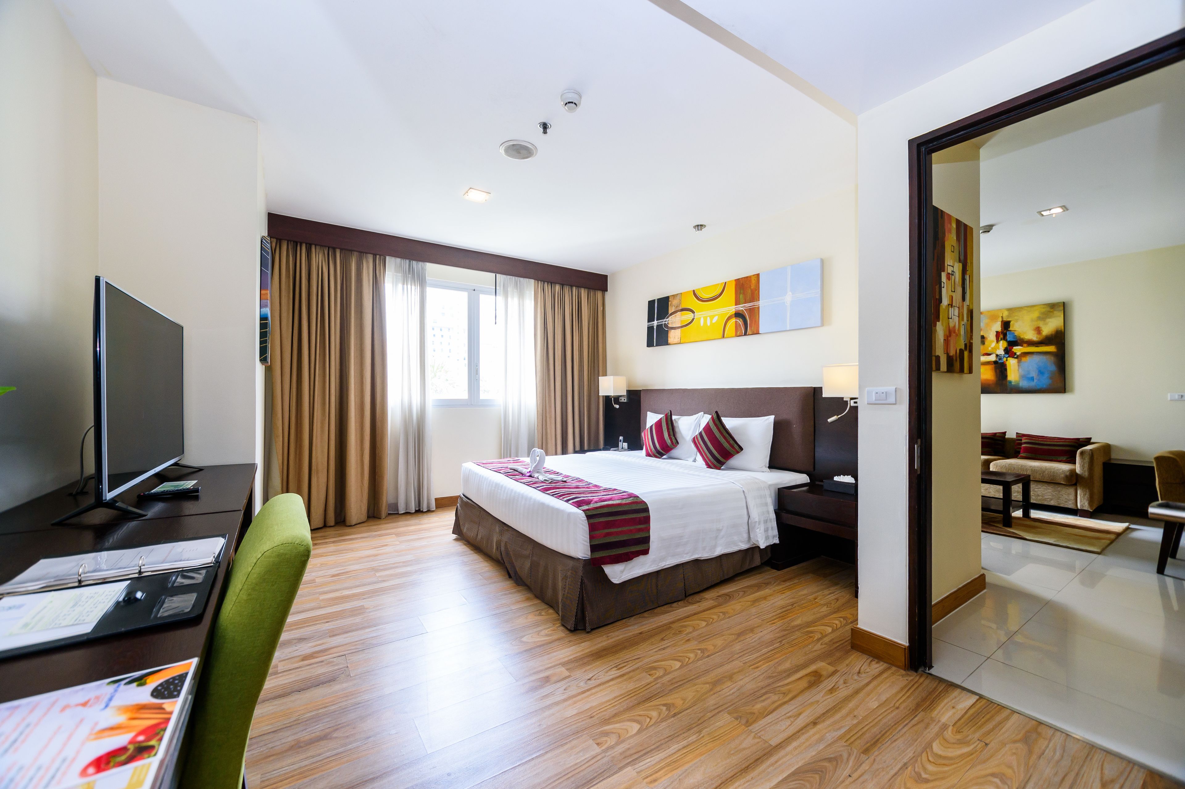 A hotel room with a bed, a desk with a computer, a television, and a dining area with a table and chairs.