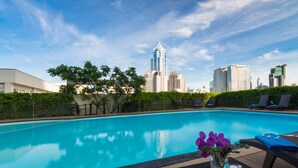 A swimming pool with a city skyline in the background, surrounded by greenery and lounge chairs. - Lohas Residences Sukhumvit (Bangkok)