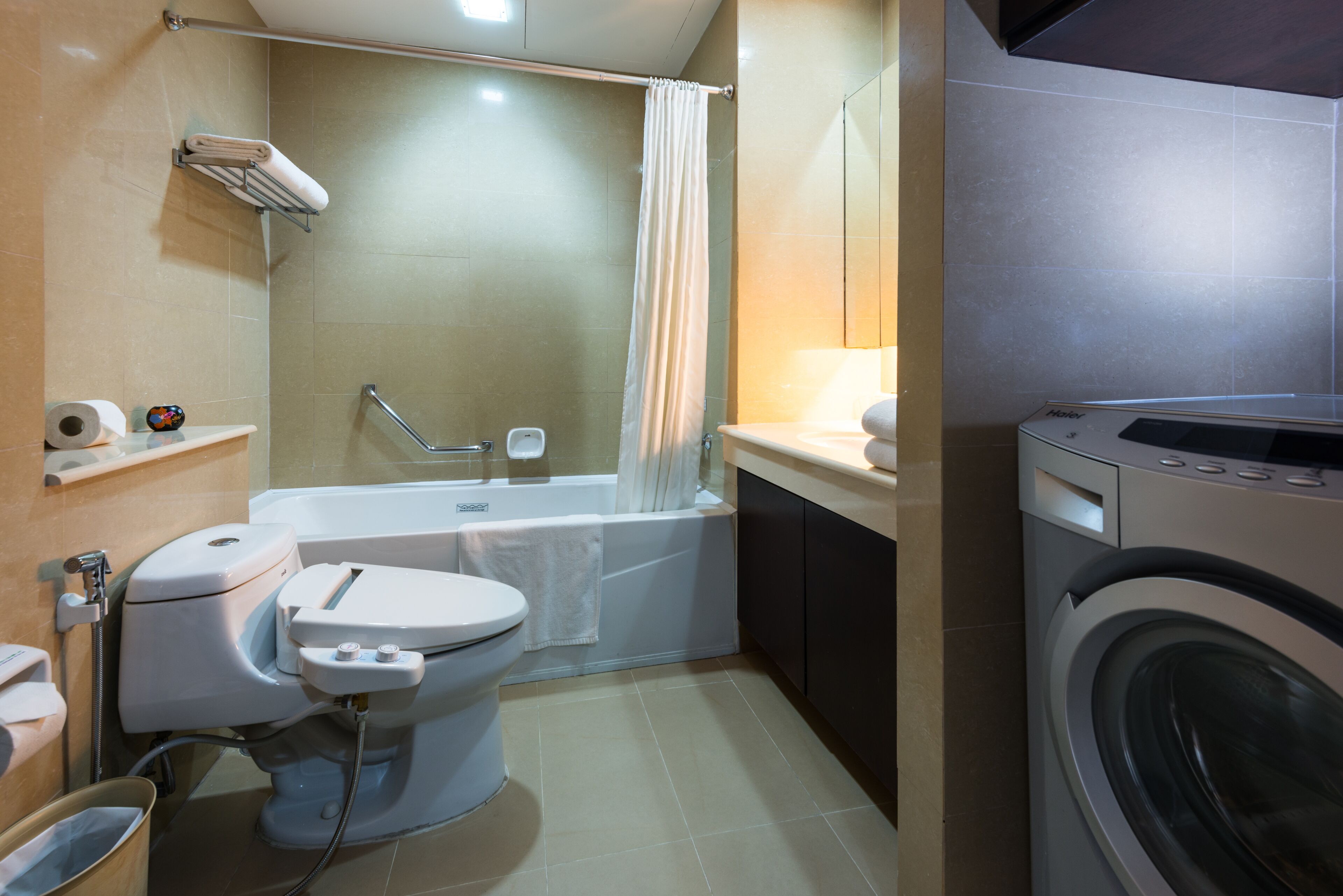 Een badkamer met toilet, bad en wasmachine.