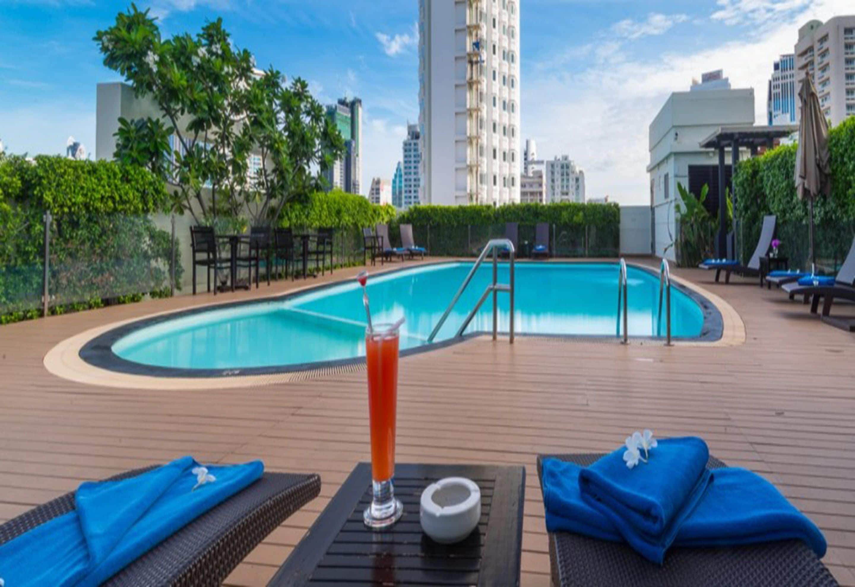 A rooftop pool area with lounge chairs, a drink, and a view of the city skyline.
