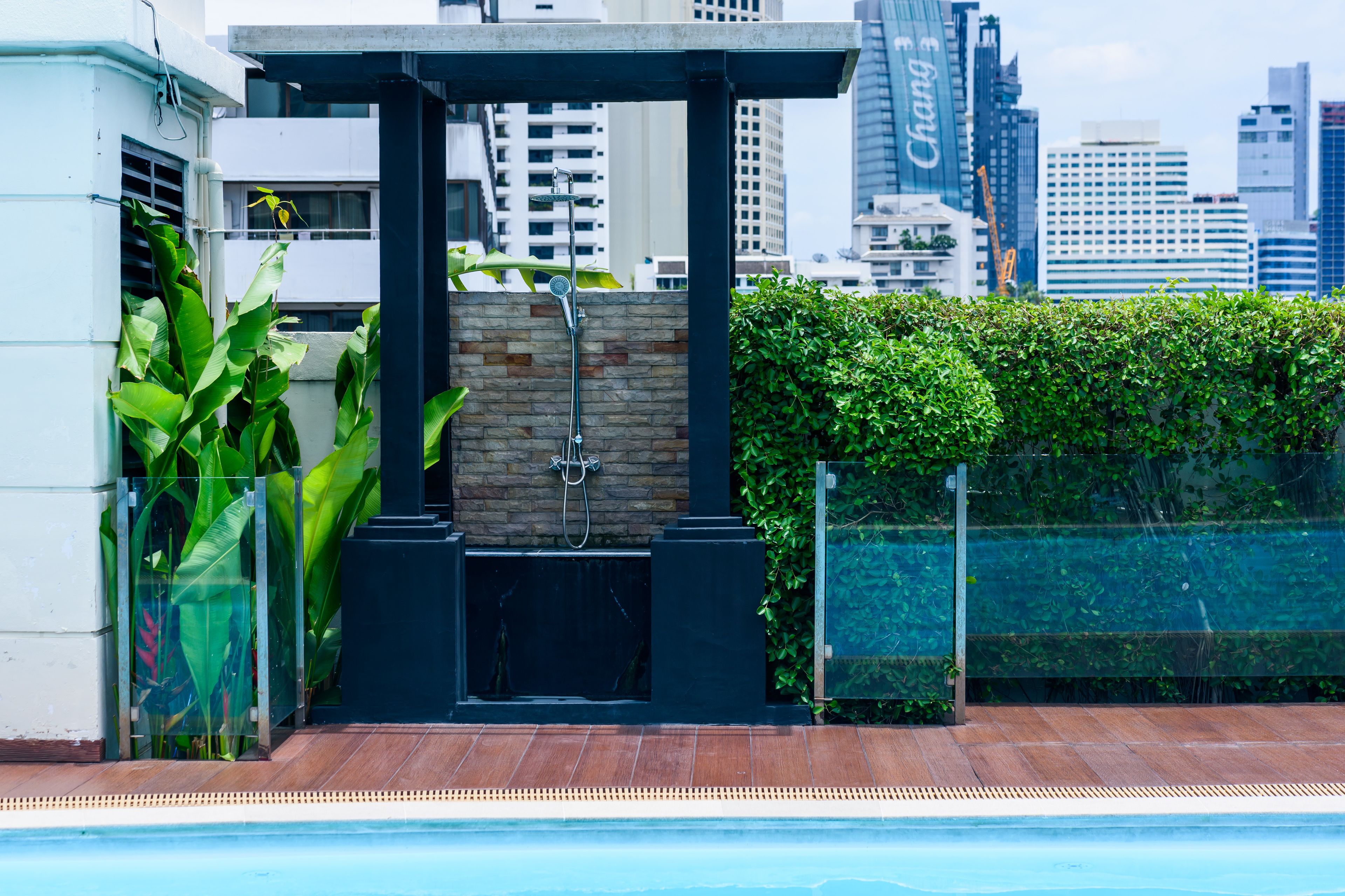 A rooftop pool area with a stone wall, a glass enclosure, and a view of city buildings.