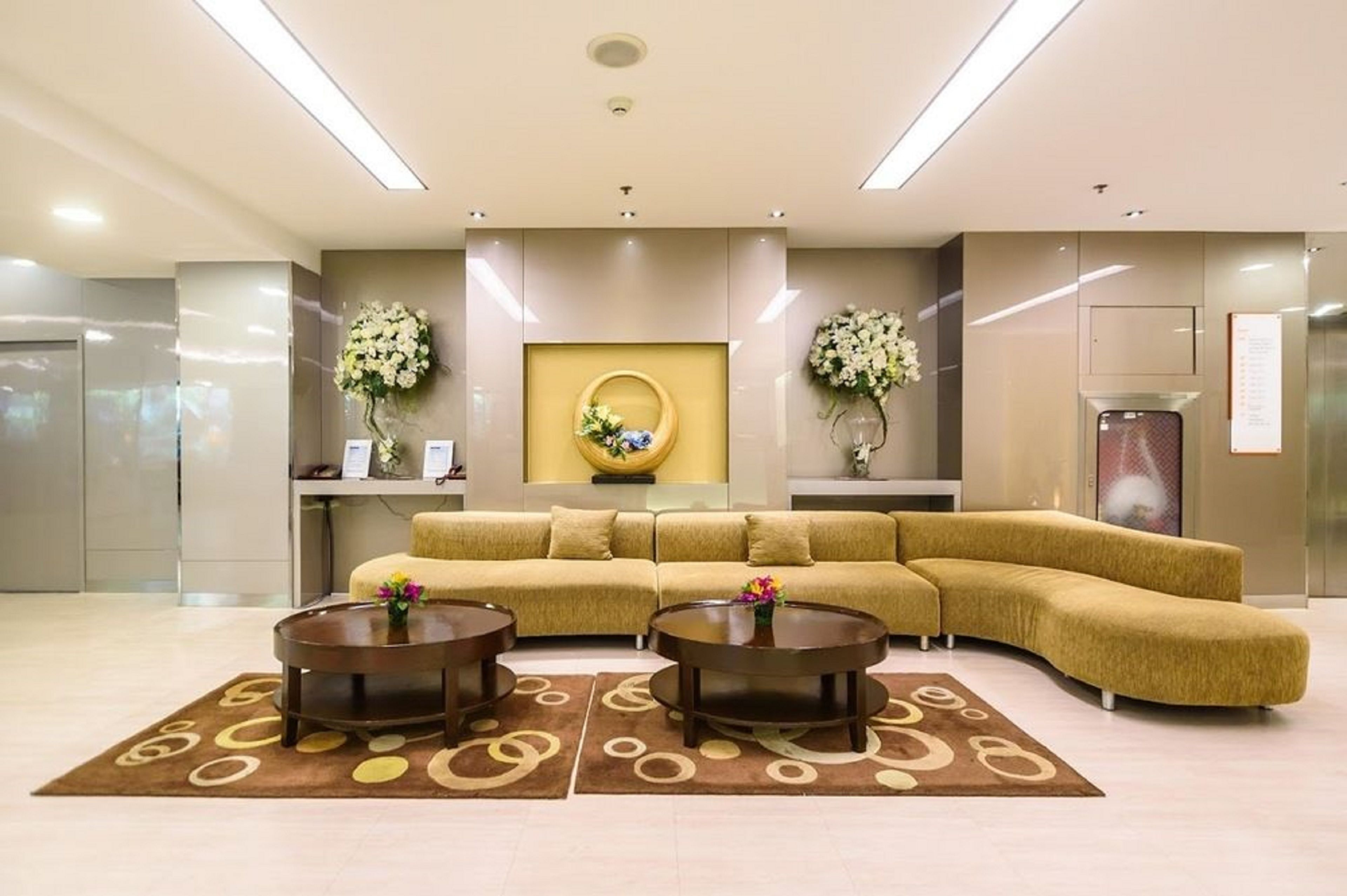 A modern lobby with a curved sofa, two round coffee tables, and decorative floral arrangements.