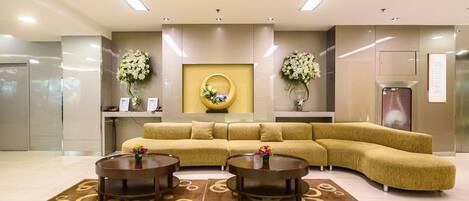 A modern lobby with a curved sofa, two round coffee tables, and decorative floral arrangements.