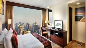 A hotel room with a large bed, a desk with a computer, a TV, and a city view. - Lohas Residences Sukhumvit (Bangkok)