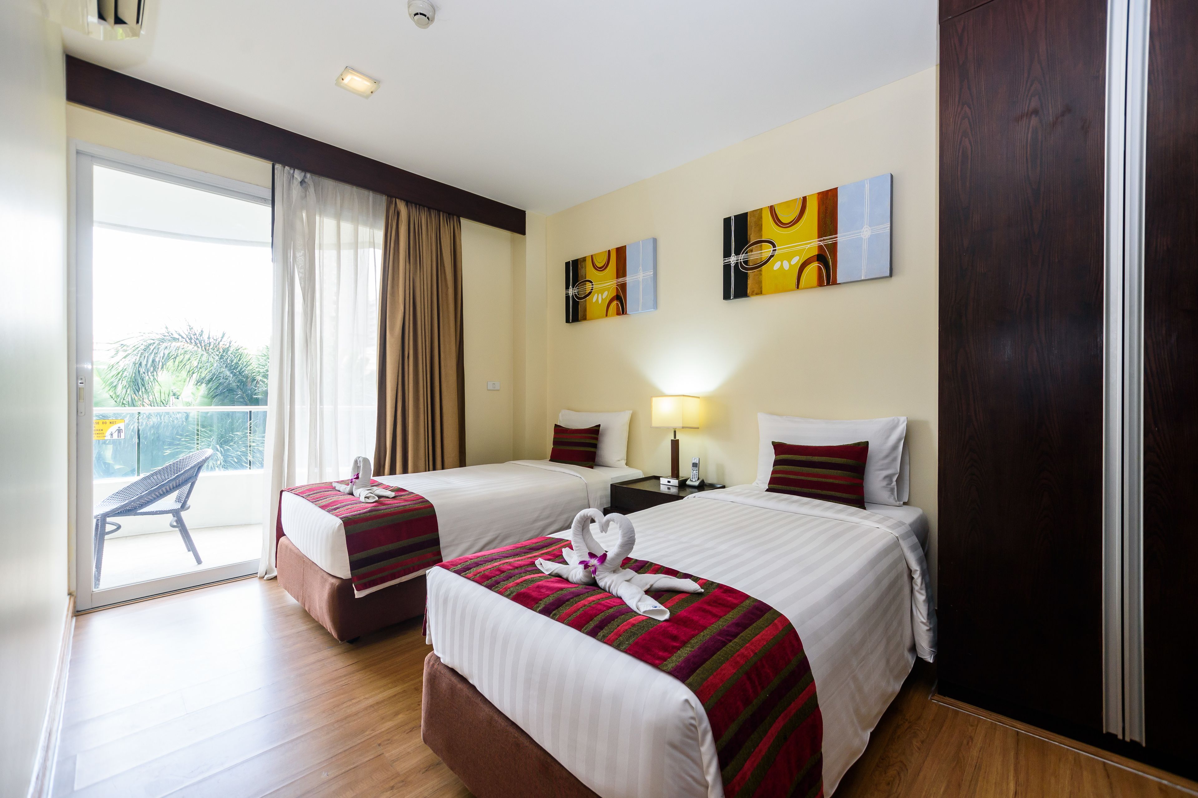 A hotel room with two beds, a balcony, and artwork on the walls.