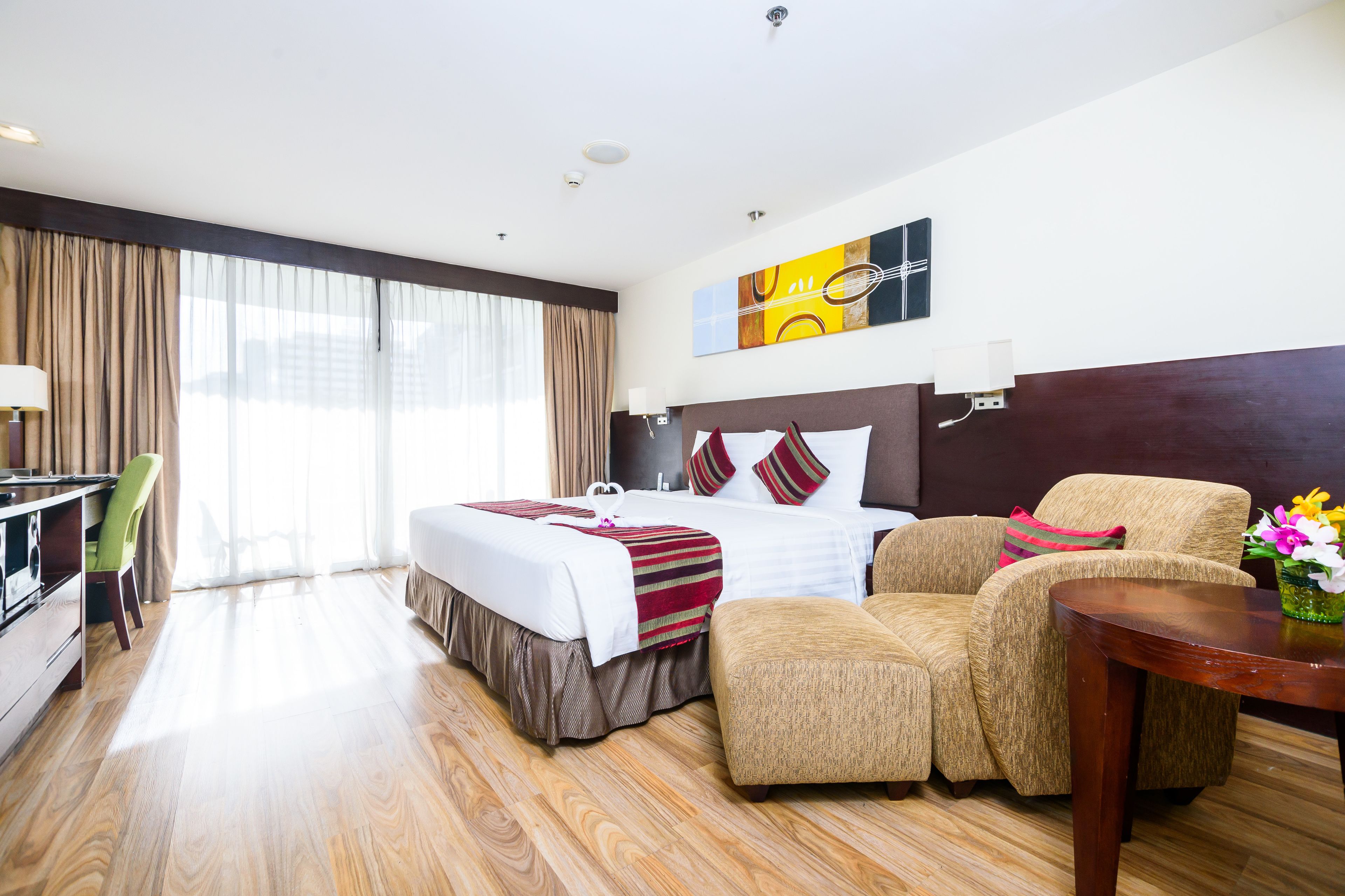 A hotel room with a large bed, a desk, a chair, and a small table with flowers.