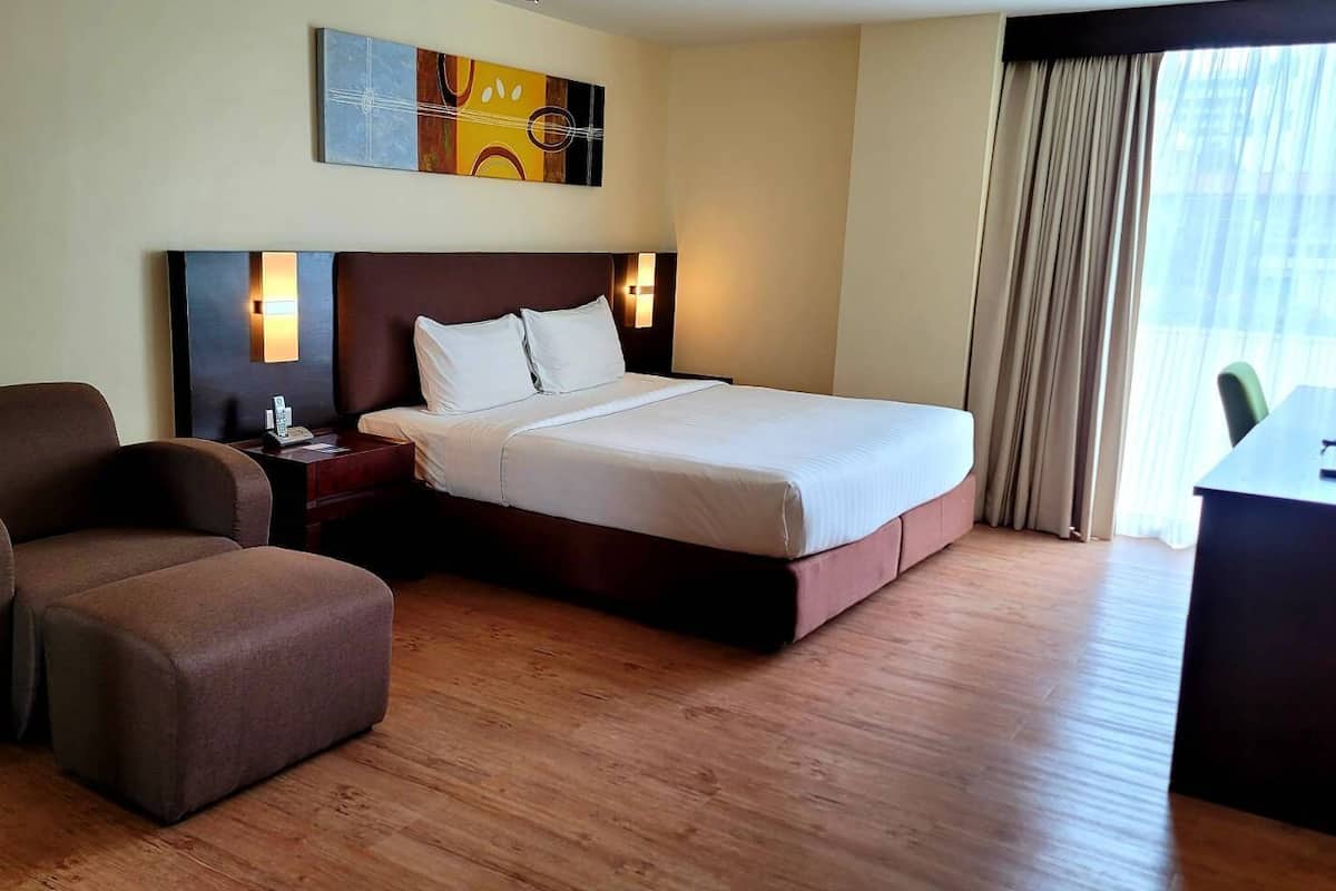 A hotel room with a bed, a chair, a desk, and a painting on the wall.
