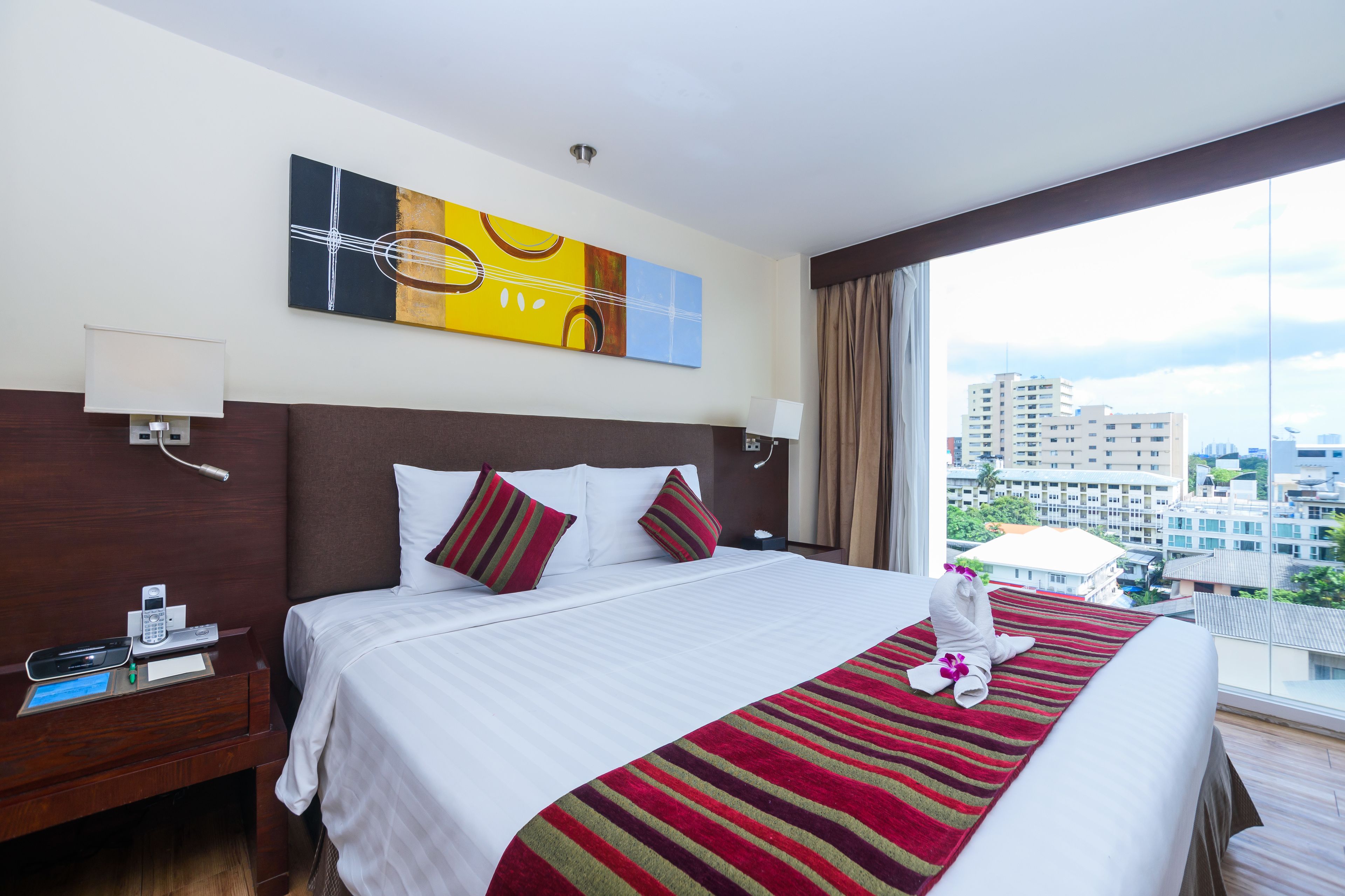 A hotel room with a large bed, a city view, a painting on the wall, and a window with curtains.