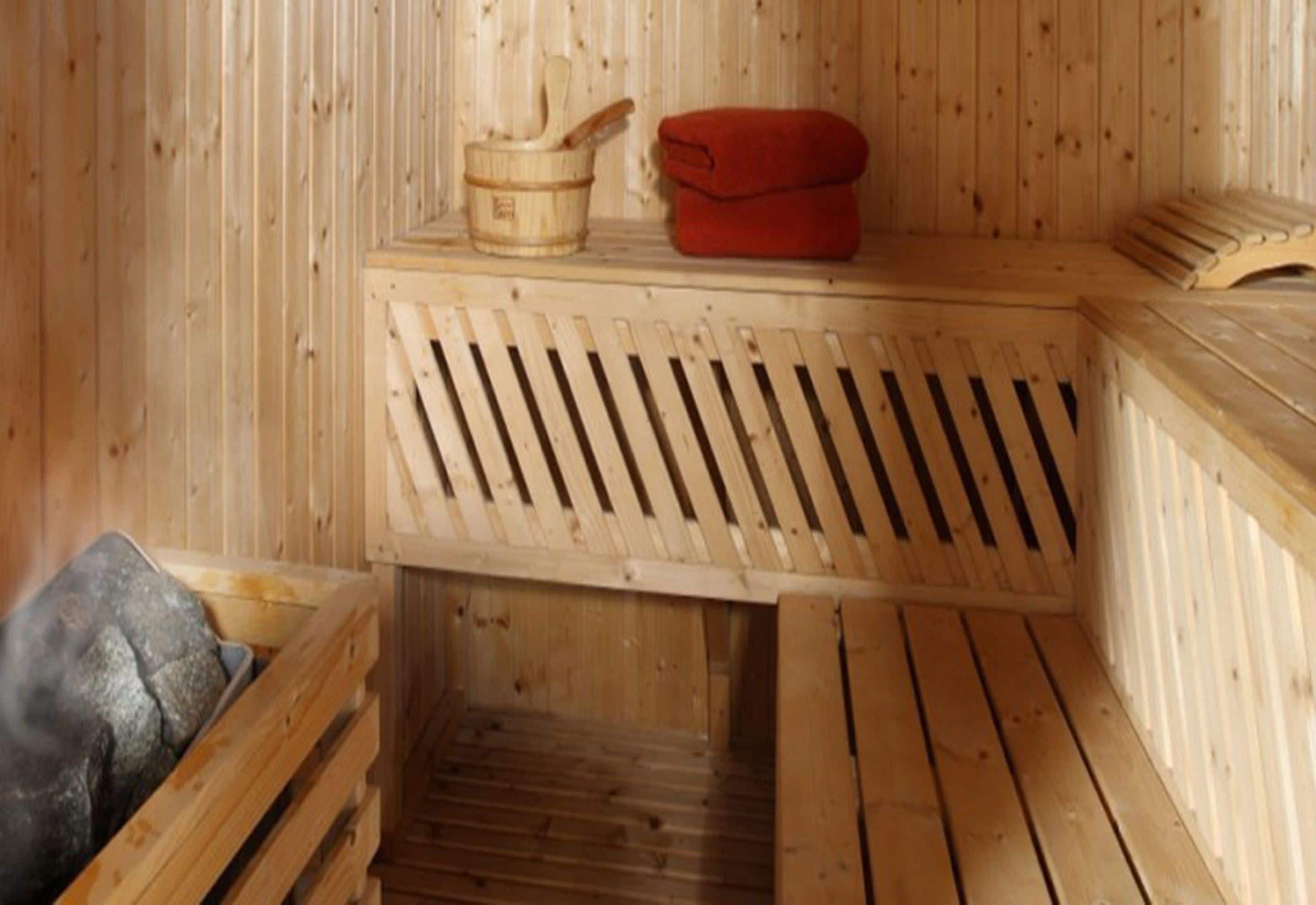 Una sauna de madera con bancos, un balde de madera y una toalla roja.