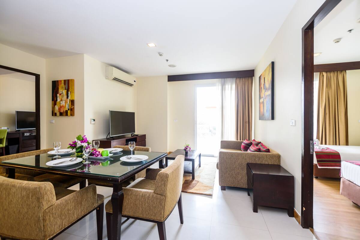 A hotel room with a dining area, a sofa, a bed, and a TV.