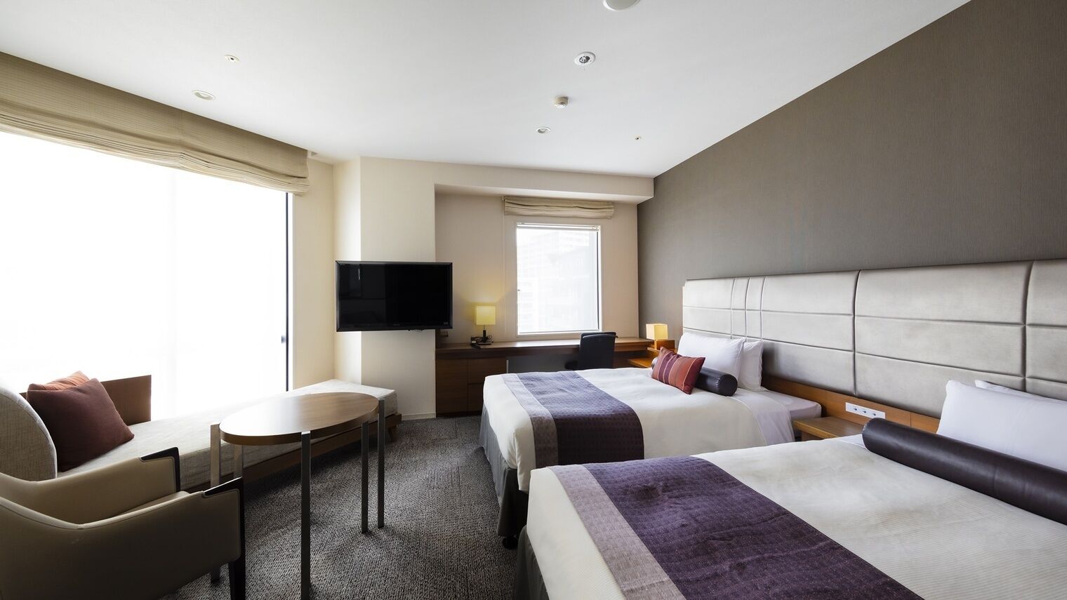 Une chambre d’hôtel avec deux lits, un bureau, une chaise, une télévision et une fenêtre.