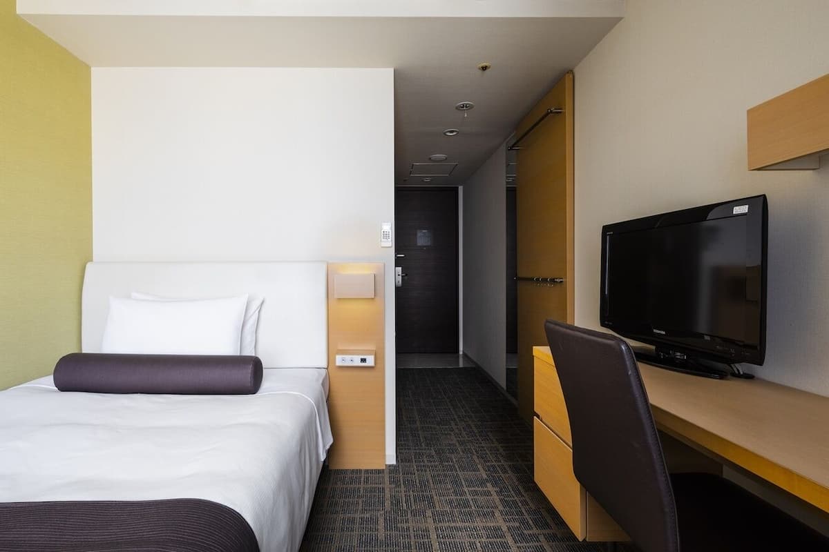 Une chambre d’hôtel avec un lit, un bureau avec une télévision et une porte donnant sur un couloir.
