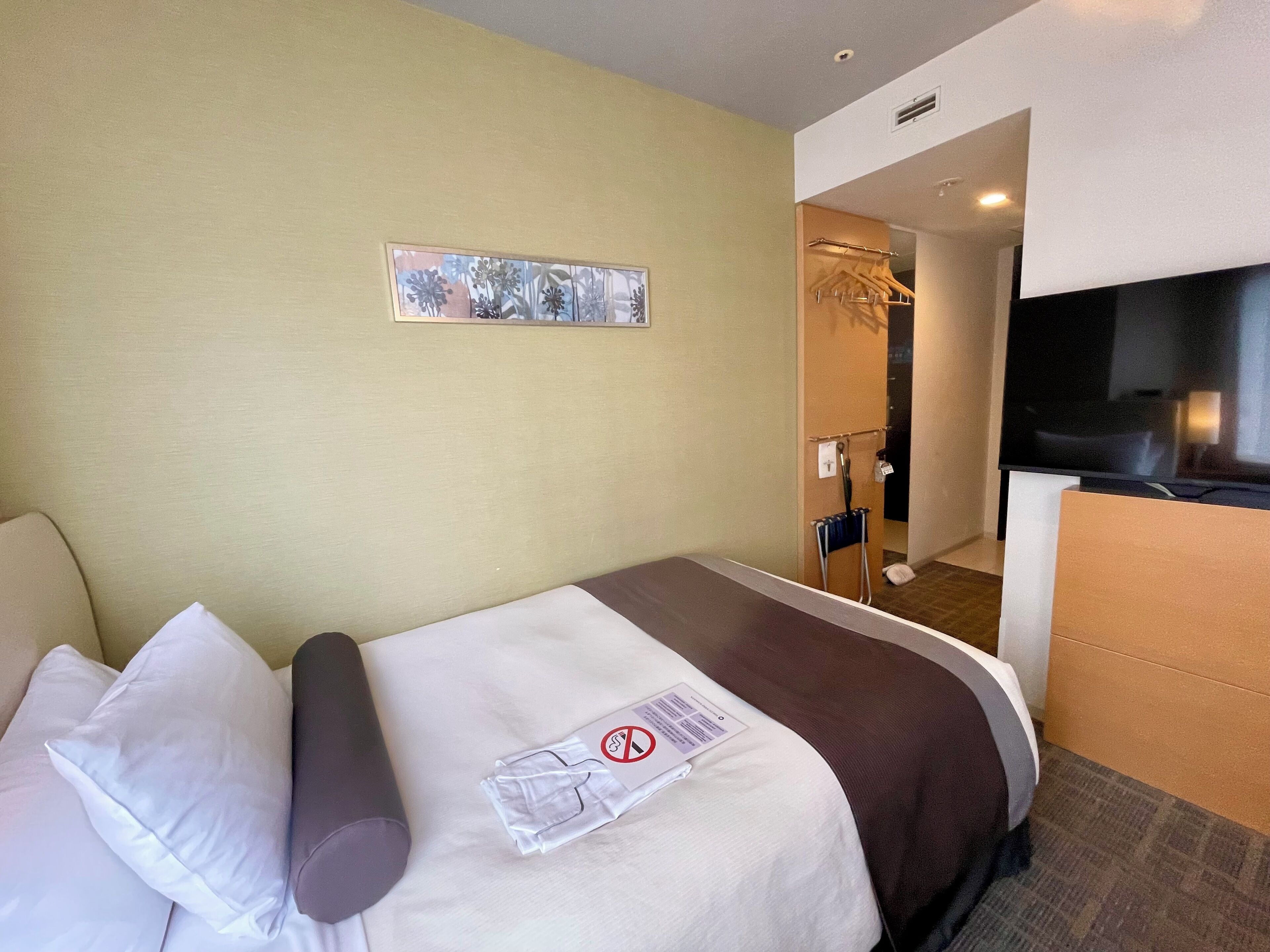 Une chambre d’hôtel avec un lit, des oreillers, une couverture, une télévision et un tableau au mur.