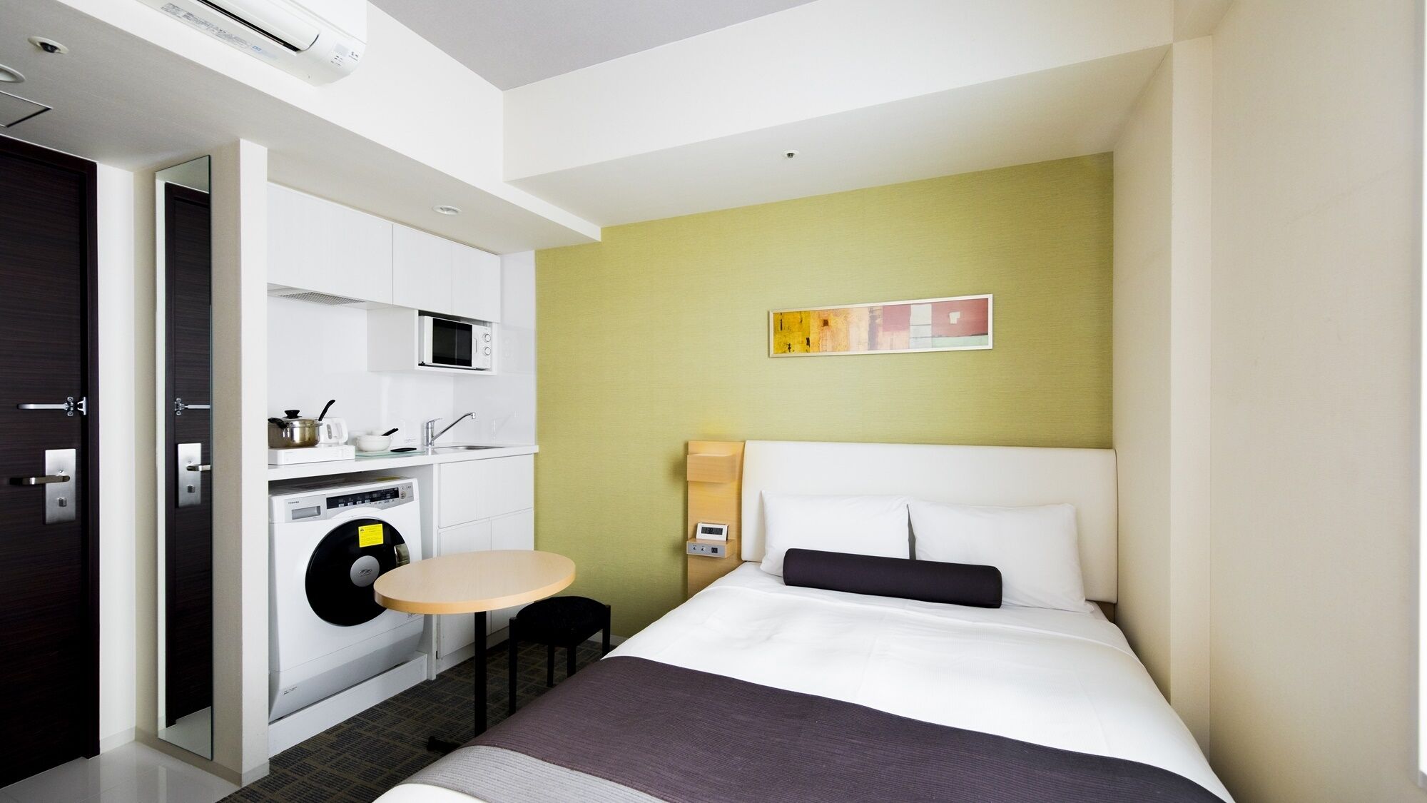Une chambre d’hôtel de taille réduite, comprenant un lit, une petite table, un four à micro-ondes, un lave-linge et un évier.