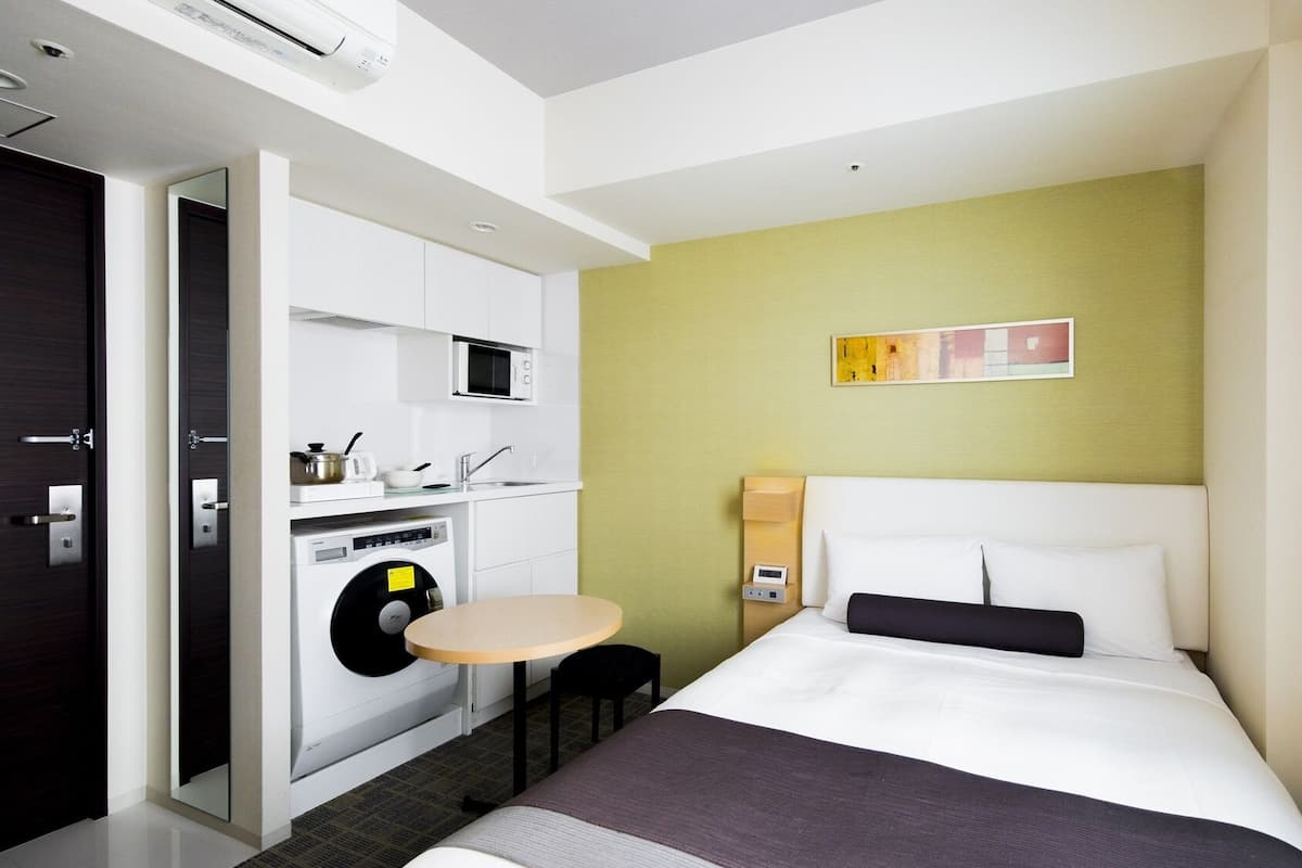 Une chambre d’hôtel de taille réduite, comprenant un lit, une petite table, un four à micro-ondes, un lave-linge et un évier.
