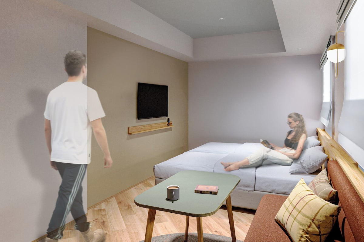 A modern room with a bed, a small table, a television mounted on the wall, and a window providing natural light.