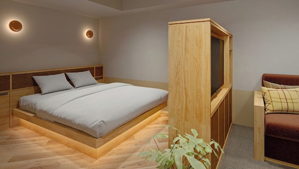 A modern bedroom with a wooden bed frame, a built-in TV, and a small seating area. - Tokyu Stay Gotanda (Tokyo)