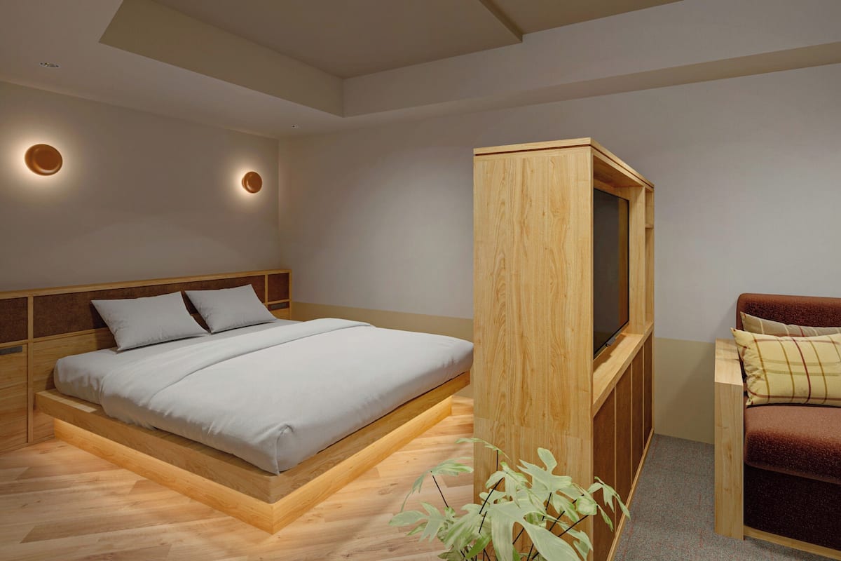 A modern bedroom with a wooden bed frame, a built-in TV, and a small seating area.