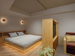 A modern bedroom with a wooden bed frame, a built-in TV, and a small seating area. - Tokyu Stay Gotanda (Tokyo)