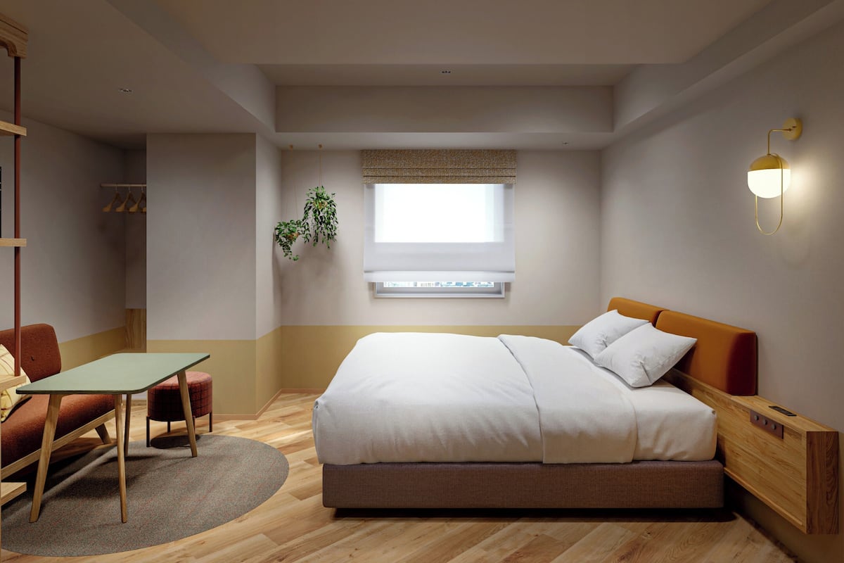 A bedroom with a bed, a desk, a chair, a hanging plant, and a window.