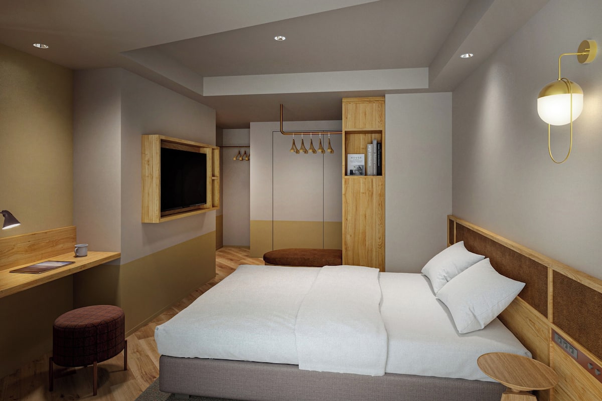 A modern hotel room with a large bed, a desk, a television, and a wardrobe.