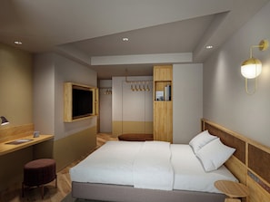 Una habitación de hotel moderna con una cama grande, un escritorio, un televisor y un armario.