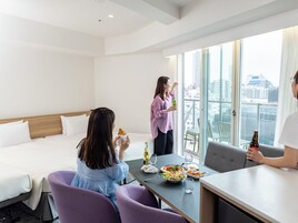 A hotel room with a dining area, a bed, and a view of the city.