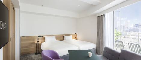 A hotel room with a large bed, a desk, purple chairs, a green table, and a city view.