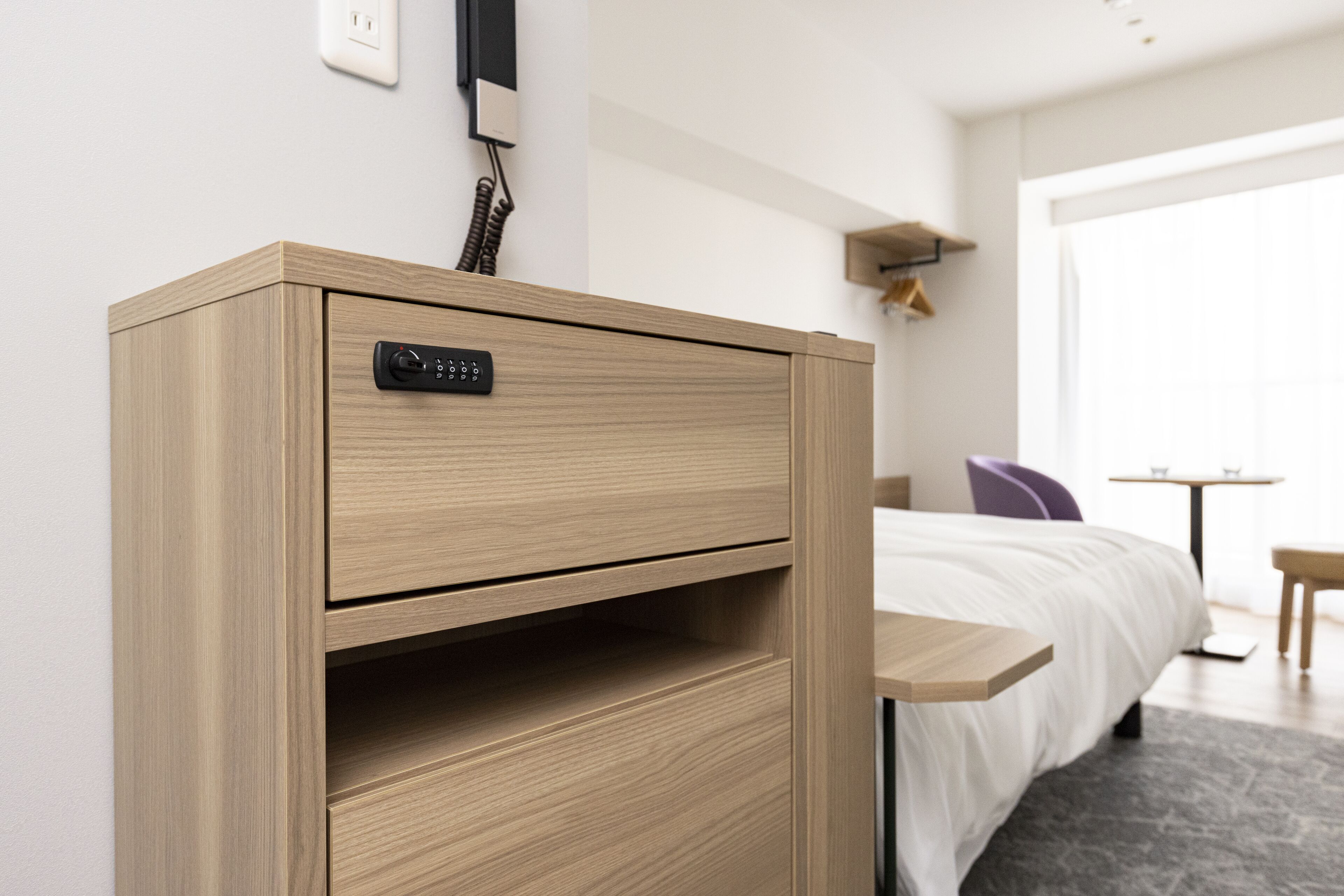 Une chambre d’hôtel avec une armoire en bois, une table de chevet, un lit avec du linge de lit blanc, une petite table et une fenêtre avec des rideaux.