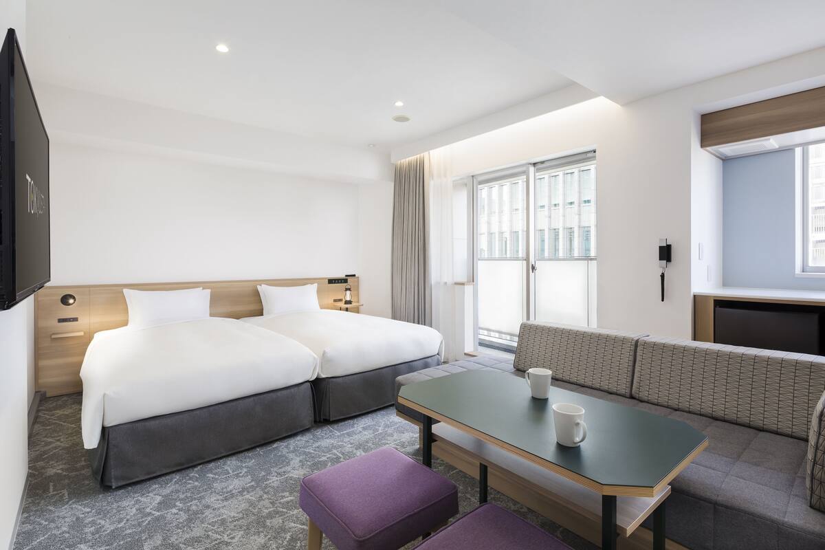A hotel room with two beds, a sofa, a table, and a TV.