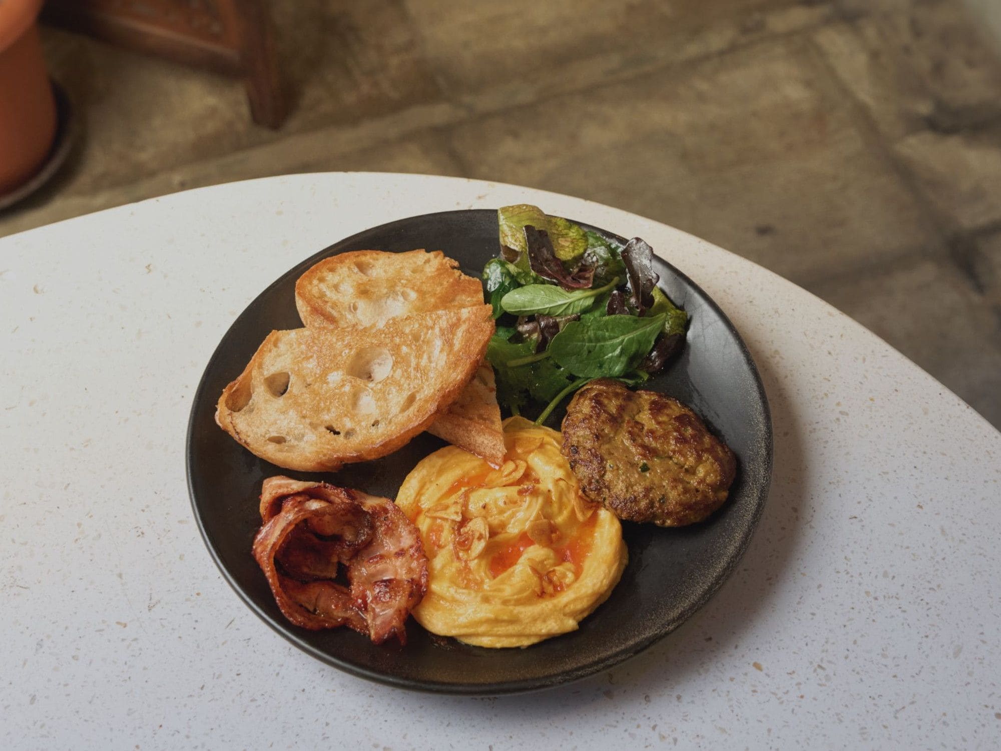 Um prato com torradas, salada, ovos mexidos, bacon e um hambúrguer.