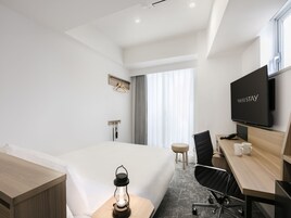 Una habitación de hotel moderna con una cama, un escritorio con silla, un televisor y una pequeña mesa con un farol.