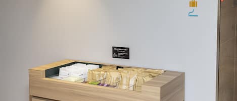 A hotel reception area with a wooden desk displaying various amenities. There is a wall-mounted sign with directional arrows and icons indicating facilities such as restrooms, a computer, and a restaurant.