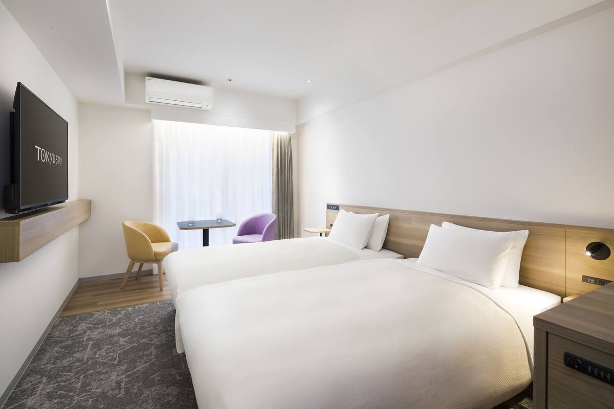 A hotel room with two beds, a TV, a desk, and a chair.