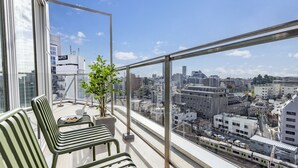 A balcony with a view of a cityscape, a potted plant, and two striped benches. - Tokyu Stay Shibuya Shin-minamiguchi (Tokyo)