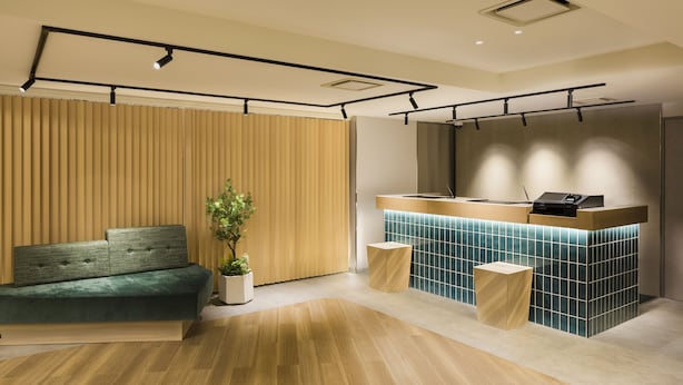 A modern reception area with a wooden reception desk, a green sofa, and a potted plant. - Tokyu Stay Shibuya Shin-minamiguchi (Tokyo)