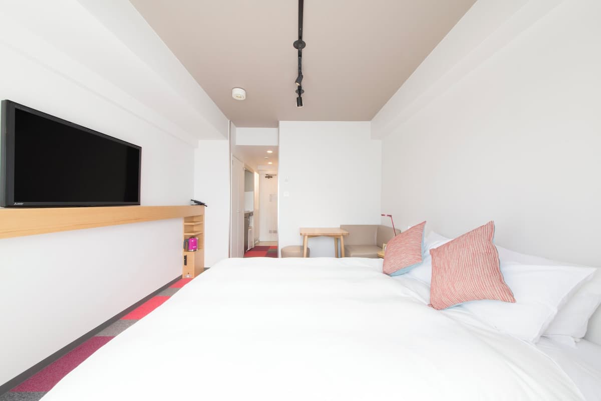 A modern hotel room with a large bed, a flat-screen TV mounted on the wall, a small table, and a chair.