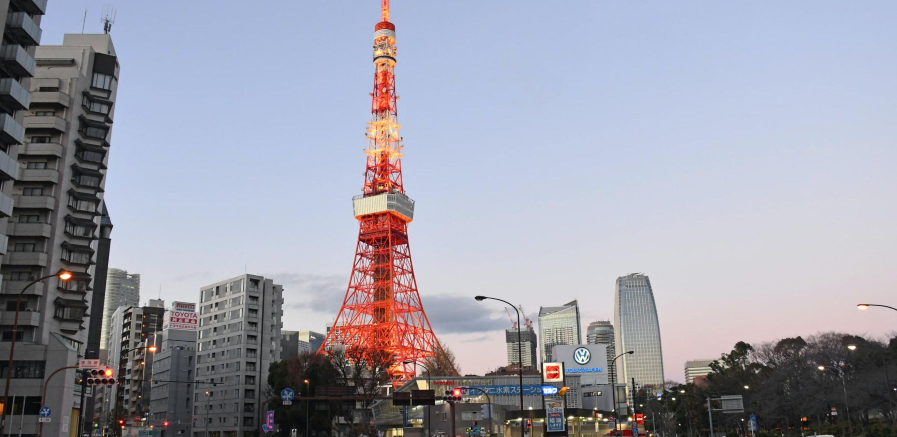 A cityscape with a prominent red tower, likely a broadcasting tower, surrounded by modern buildings and commercial signage.
