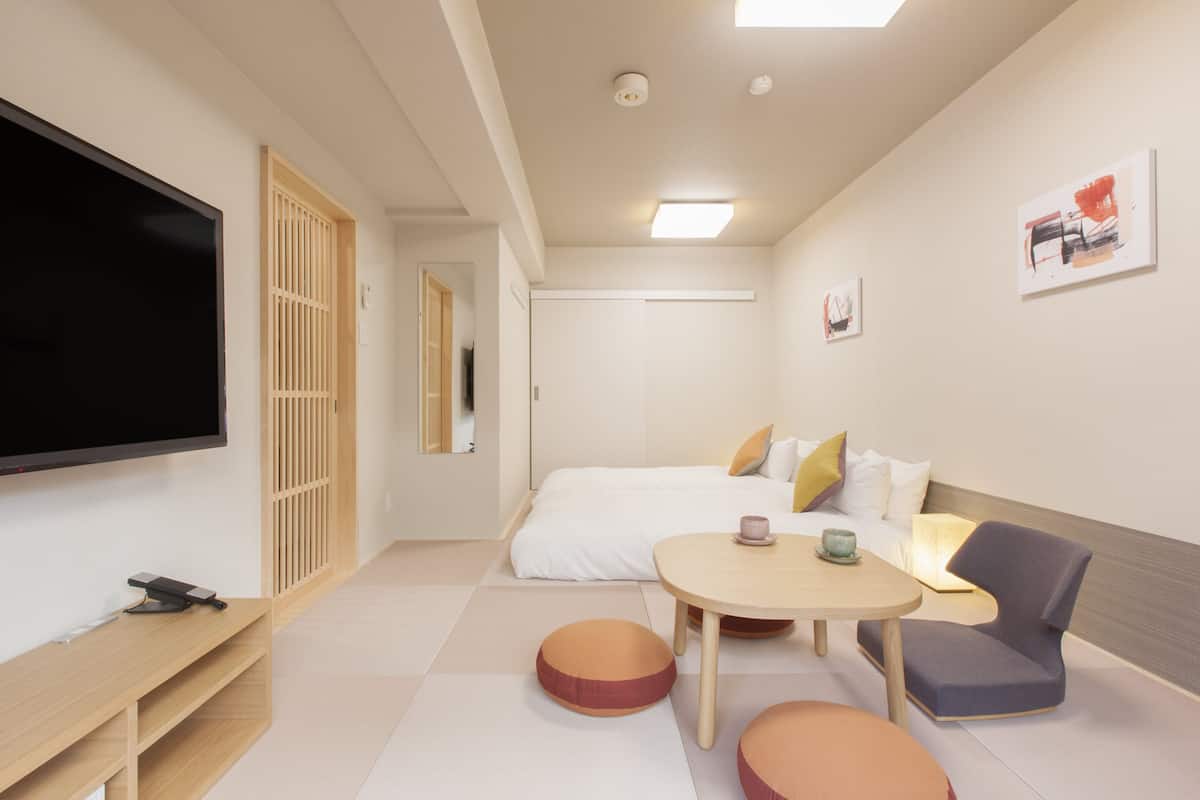 A modern hotel room with a flat-screen TV, a wooden console table, a round table with a cup, a sofa, and a chair.