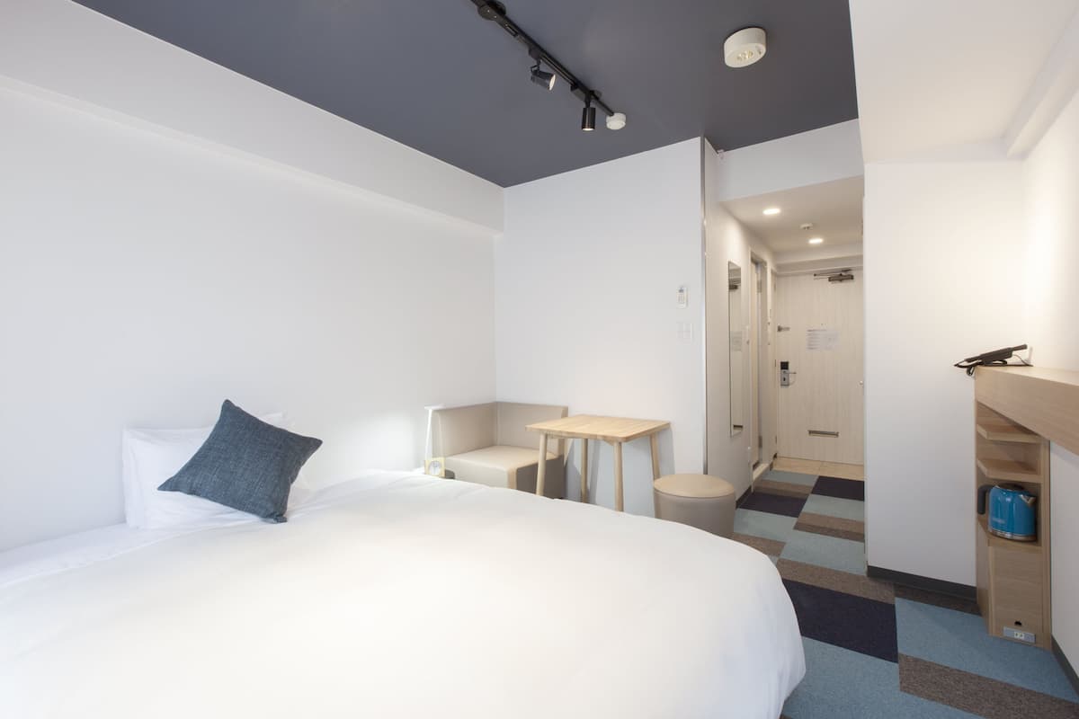 A hotel room with a large bed, a small table, a chair, and a desk with a computer.