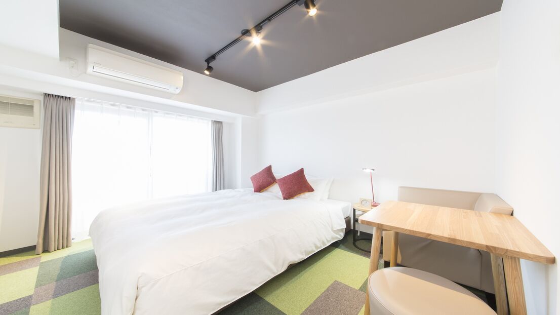 A hotel room with a bed, a desk, a chair, and a window with curtains.