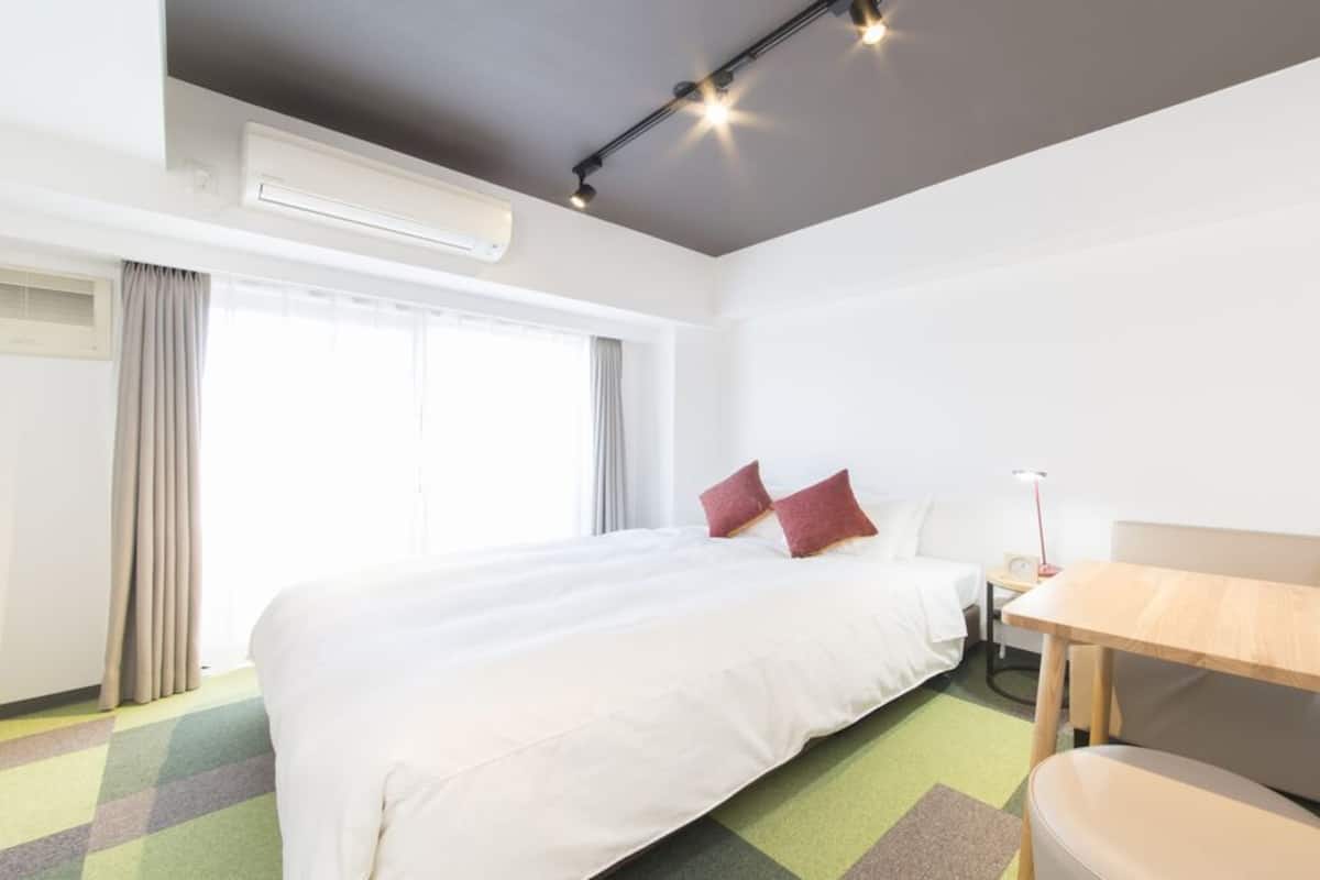 A hotel room with a bed, a desk, a chair, and a window with curtains.