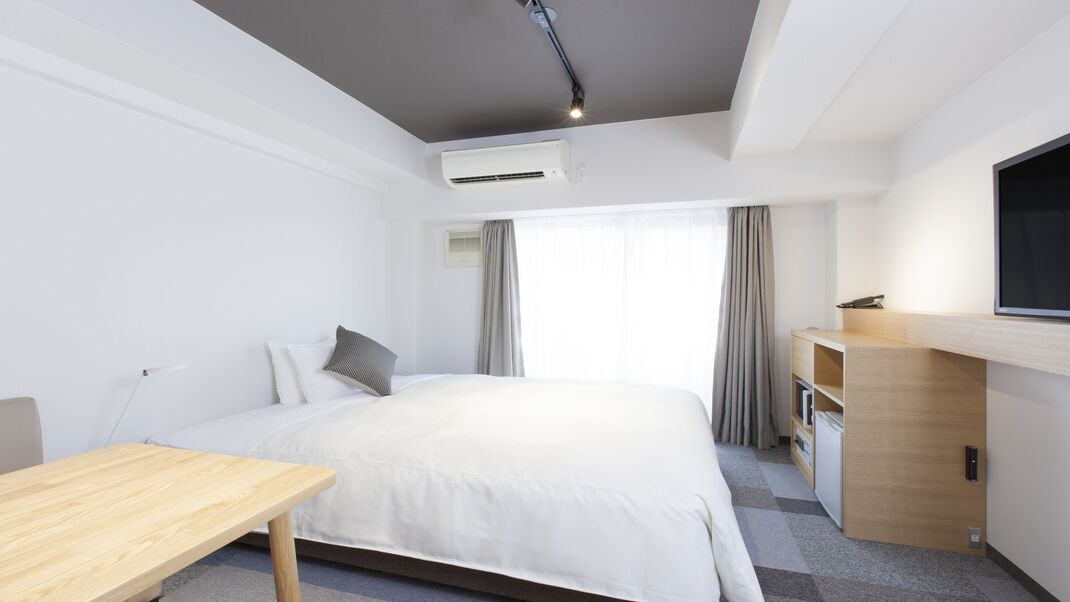 A hotel room with a bed, a desk, a TV, and a wardrobe.