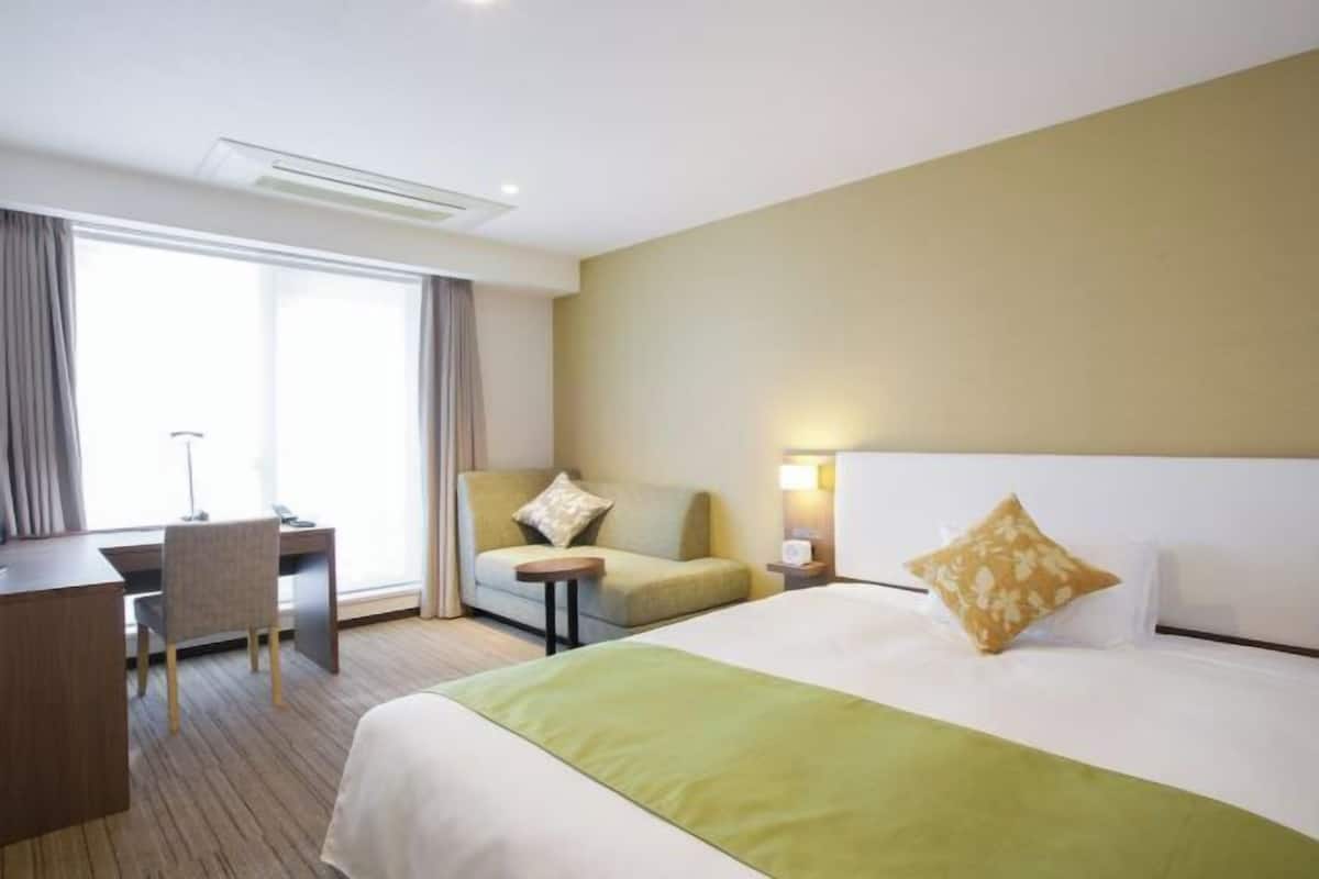 Relax in a spacious room with a large bed, desk, and comfortable armchair, offering a view of the outdoors.