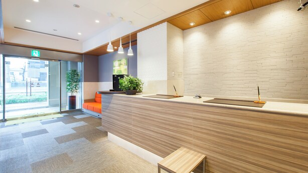 A modern reception area with a wooden counter, a potted plant, and a bench. - Tokyu Stay Yoga (Tokyo)